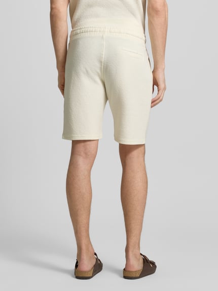 Männermodel trägt Sweatshorts mit elastischem Bund von MCNEAL, Strukturmuster, gerade Passform, Eingriff- und Gesäßtaschen, Ganzkörperansicht Rückansicht.