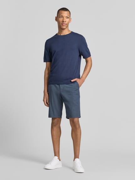 Männermodel trägt Bermudas mit Gürtel und Gesäßleistentaschen von Christian Berg Men aus Baumwoll-Mix mit Stretch-Anteil in Blau, Ganzkörperansicht von vorne. Passform: Straight Fit; Details: Knopf- und Reißverschluss, Gürtel, französische Eingrifftaschen; Bundweite bei Größe 50: 45 cm, Innenbeinlänge bei Größe 50: 28 cm.