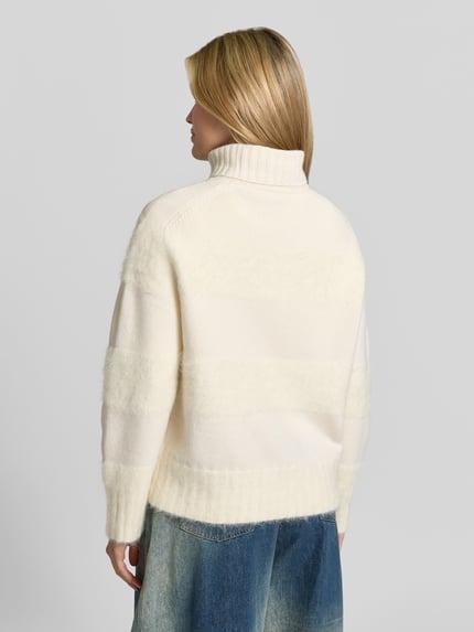 Frauenmodel trägt Pullover aus Alpaka mit Rollkragen Modell 'Mila' von Joseph in cremefarbener Strickoptik mit Struktur und Ripp, Ganzkörperansicht Rückansicht.