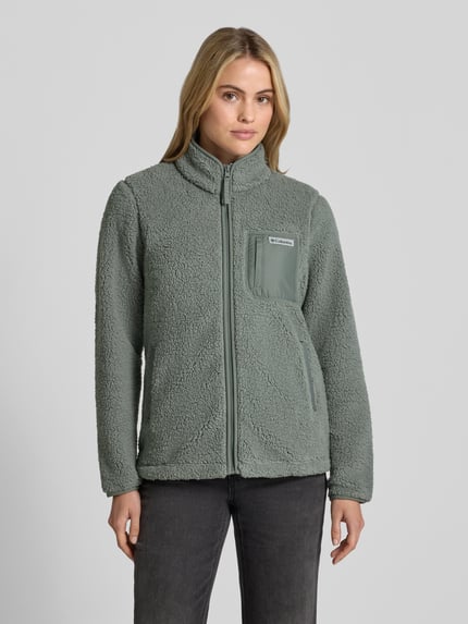Frauenmodel trägt Fleecejacke mit Stehkragen und Label-Detail von Columbia in Grün, strukturierter Stoff, Reißverschluss, Regular Fit, Ganzkörperansicht von vorne. Rückenlänge 65 cm, Schulterbreite 41 cm, Brustweite 50 cm, Ärmellänge 64 cm.