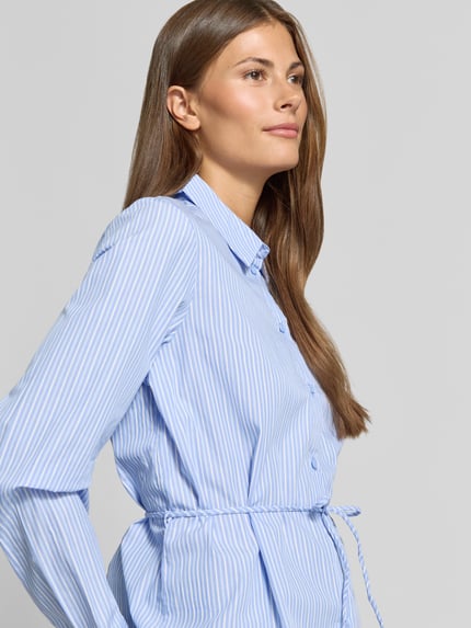 Frauenmodel trägt Regular Fit Hemdbluse aus reiner Baumwolle Modell 'ELINA' von VERO MODA, hellblau mit weißen Streifen, Nahaufnahme Oberkörper.