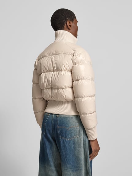 Frauenmodel trägt Funktionsjacke mit Logo-Patch Modell 'queens bomber' von Moose Knuckles in Beige, Webware mit Steppung, Ganzkörperansicht Rückansicht.