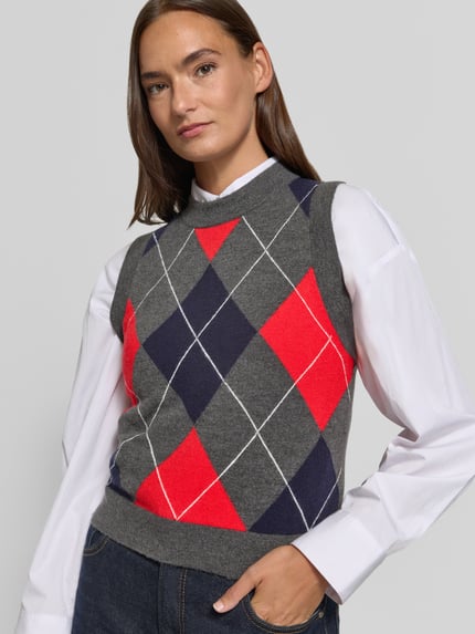Frauenmodel trägt Pullunder mit Rundhalsausschnitt Modell 'BIMBU' von MANGO im Material-Mix, grau mit roten und blauen Rauten, Nahaufnahme Oberkörper.