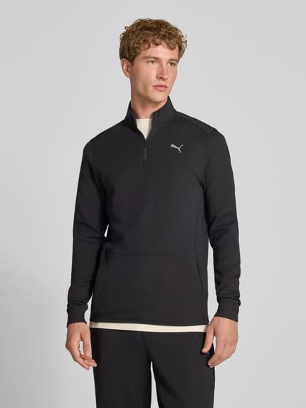 Męski model nosi bluzę Sweatshirt mit Label-Detail Modell 'CLOUDSPUN' od PUMA PERFORMANCE, elastyczna mieszanka materiałów z lyocellem, prosty krój, kołnierz zapinany, detal z logo, długość tyłu w rozmiarze M: 74 cm, długość rękawów w rozmiarze M: 74 cm, kolor czarny, gładka faktura, całkowity widok od przodu.