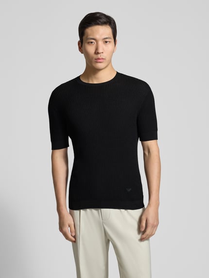 Männermodel trägt Slim Fit T-Shirt mit Seiden-Anteil in Strick-Optik von Emporio Armani, Schwarz, Baumwoll-Mix, Ganzkörperansicht von vorne.