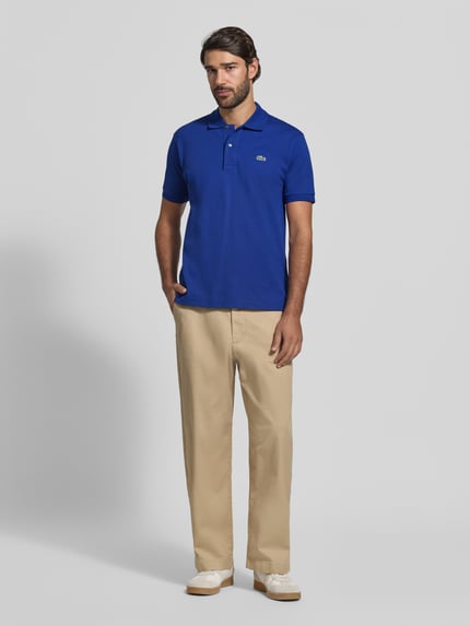 Männermodel trägt Regular Fit Poloshirt aus reiner Baumwolle von Lacoste in kräftigem Blau, glatte Textur, Ganzkörperansicht von vorne.