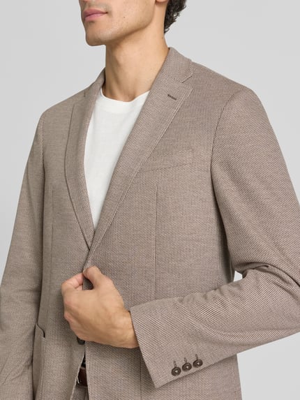 Männermodel trägt fein strukturiertes Slim Fit 2-Knopf-Sakko Modell 'Michel' von Pierre Cardin in Beige mit Reverskragen, Nahaufnahme Oberkörper. Herren 2-Knopf-Sakko, Material-Mix mit Viskose-Anteil, aufgesetzte Taschen.