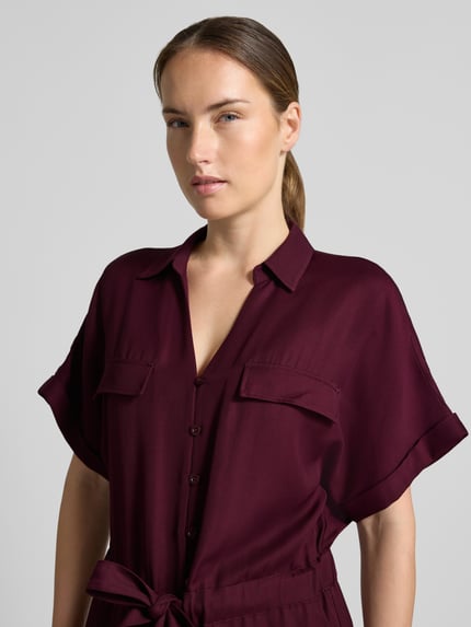 Frauenmodel trägt Jumpsuit aus Viskose-Lyocell-Mix von MORE & MORE in Dunkelrot mit Umlegekragen, Taillenband, Nahaufnahme Oberkörper.