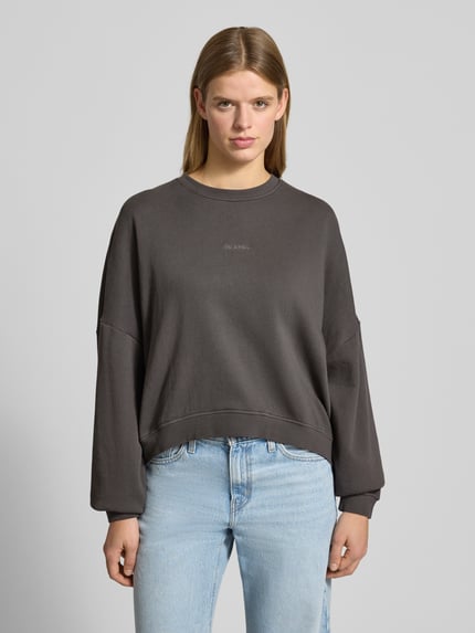 Frauenmodel trägt Oversized Sweatshirt mit Label-Stitching von OH APRIL aus reiner Baumwolle, anthrazitfarben, Rundhalsausschnitt, Nahaufnahme Oberkörper.