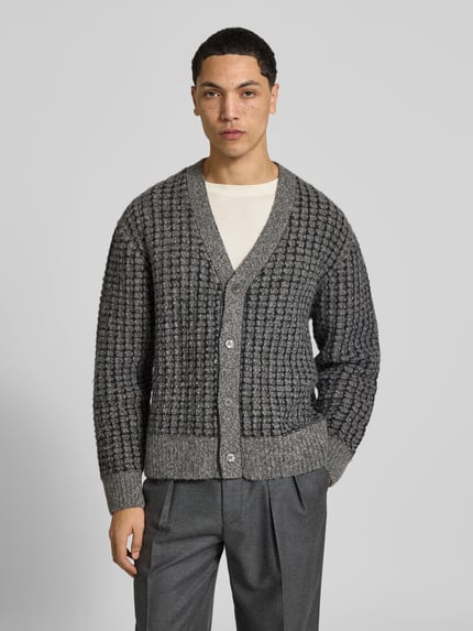 Männermodel trägt Strickjacke mit Bouclé-Strukturoptik von Officine Générale in grau melierter Strickoptik, Knopfleiste, Ganzkörperansicht von vorne.