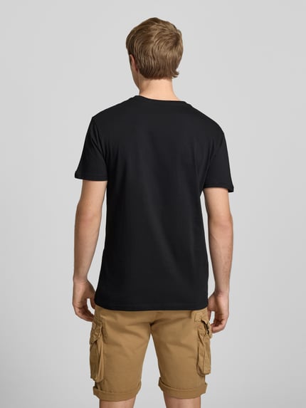 Männermodel trägt T-Shirt mit Logo und Rundhalsausschnitt von Alpha Industries aus Reine Baumwolle, Regular-Fit, Rückenlänge 68 cm, Ganzkörperansicht Rückansicht.