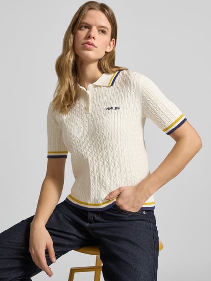 Frauenmodel trägt Regular Fit Poloshirt mit Zopfmuster und Logo-Stitching von Karo Kauer aus Viskose-Mix mit Polokragen und kurzer Knopfleiste, creme mit farbigen Bündchen, Rückenlänge bei Größe S 52 cm, Ärmellänge 23 cm, Nahaufnahme Oberkörper.