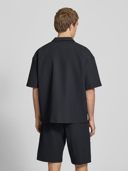 Männermodel trägt schwarzes Relaxed-Fit Freizeithemd mit Reverskragen Modell 'Troy' von Pegador, Strukturmuster, Ganzkörperansicht Rückansicht. Rückenlänge bei Größe M 67 cm, Schulterbreite 49 cm, Ärmellänge 24 cm, Kurzärmelig, durchgängige Knopfleiste, Logo-Stitching.
