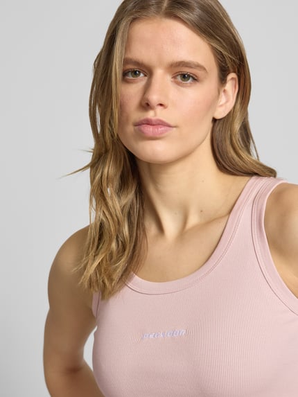 Vrouwenmodel draagt Tanktop met Logo-Print model 'Cesis' van Pegador in lichtroze katoenmix met stretch, fijnrib, nauwsluitend model, logoprint, ronde hals, detailopname bovenlichaam.