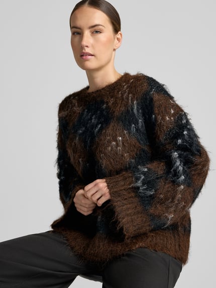 Frauenmodel trägt Relaxed Fit Strickpullover aus Woll-Mix von Neo Noir, braun-schwarz kariert, elastisch, Rundhals, Langarm, Nahaufnahme Oberkörper.