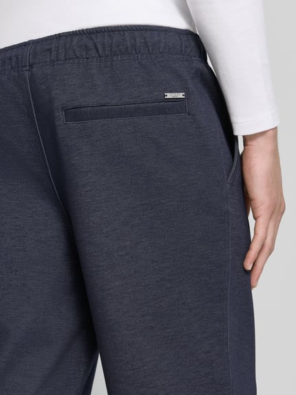 Männermodel trägt Straight Fit Stoffhose aus elastischem Viskose-Mix von GUESS in Dunkelblau, elastischer Bund, Detailaufnahme Rückansicht.