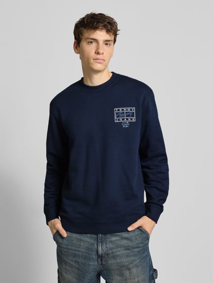 Männermodel trägt Regular Fit Sweatshirt aus reiner Baumwolle von Tommy Jeans in Dunkelblau mit Label Print, Ganzkörperansicht von vorne.