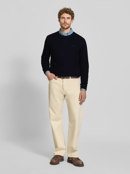 Männermodel trägt Regular Fit Pullover aus Baumwoll-Woll-Mix von GANT in Dunkelblau, kombiniert mit heller Hose, Ganzkörperansicht von vorne.