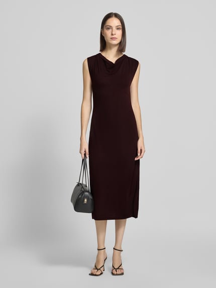 Frauenmodel trägt Strickkleid mit Wasserfall-Ausschnitt Modell 'SANTA' von MANGO, dunkle Farbe, glatte Textur, Ganzkörperansicht von vorne. Gerader Schnitt, Midikleid, Rückenlänge 113 cm, Brustweite 37 cm.