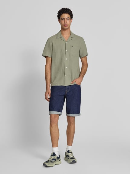 Männermodel trägt Regular Fit Jeansshorts aus Baumwoll-Mix von Tommy Jeans in dunkler Denim-Optik, sichtbare Label-Patch und 5-Pocket-Design, Ganzkörperansicht von vorne.