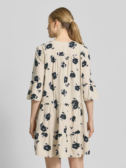 Frauenmodel trägt ausgestelltes Blusenkleid aus reiner Baumwolle Modell 'DICTHE' von Vero Moda mit Allover-Muster und Trompetenärmeln, Ganzkörperansicht Rückansicht.