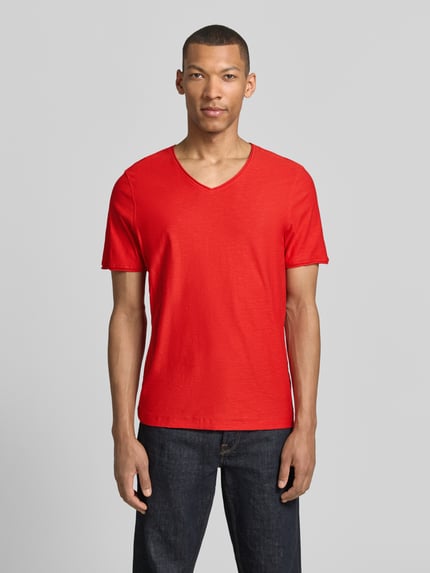 Męski model nosi Regular Fit T-Shirt mit V-Ausschnitt od MCNEAL z bawełny, krój regular fit, dekolt w serek, zrolowany brzeg, długość tyłu w rozmiarze M: 70 cm, widok całej sylwetki z przodu.