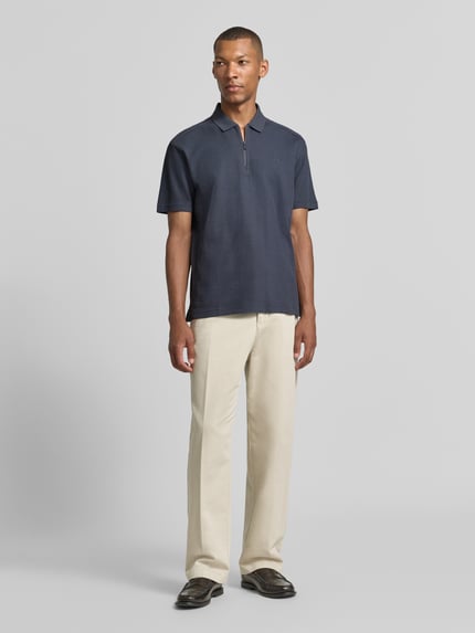 Männermodel trägt Regular Fit Poloshirt aus reiner Baumwolle Modell 'Pe_RibNylon' von BOSS, dunkelblau, mit beiger Hose, Ganzkörperansicht von vorne, Herren Poloshirt von BOSS Orange.