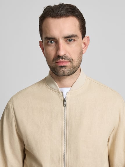 Männermodel trägt Jacke aus Baumwoll-Leinen-Mix mit Zweiwege-Reißverschluss von Jack & Jones Premium, beige, Struktur sichtbar, Nahaufnahme Oberkörper, Regular-Fit, Stehkragen, Rückenlänge 68 cm, Schulterbreite 45 cm, Brustweite 54 cm, Ärmellänge 66 cm, Größe M.