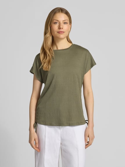 Kobieta modelka nosi t-shirt z wiązaniem z boku od Apricot, mieszanka materiałów z dodatkiem wiskozy, krój regular fit, okrągły dekolt, długość tyłu w rozmiarze S: 59 cm, zielony kolor, prosta struktura, całkowity widok z przodu.