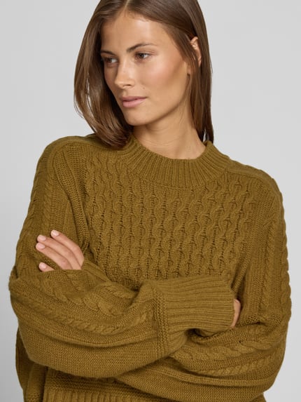Frauenmodel trägt Strickpullover mit Zopfmuster von Style Icon Collection in Olivgrün, reine Baumwolle, lockere Passform, Nahaufnahme Oberkörper.