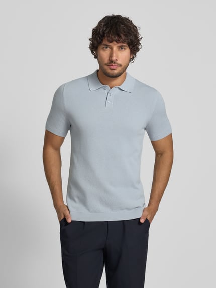 Männermodel trägt Slim Fit Poloshirt Modell 'Triton' von Drykorn, reine Baumwolle, hellblau, Strukturmuster, Polokragen, Ganzkörperansicht von vorne.