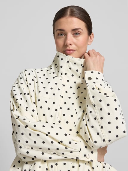 Kobiece modelka nosi kurtkę z wzorem w kropki na całej powierzchni, model 'CALLISA DOT' od Neo Noir, krój regular fit, stójka, długość tyłu w rozmiarze 36: 53 cm, szerokość ramion w rozmiarze 36: 53 cm, szerokość klatki piersiowej w rozmiarze 36: 56 cm, długość rękawów w rozmiarze 36: 54 cm, jasne tło, gładka tekstura tkaniny, nahaufnahme górnej części ciała.