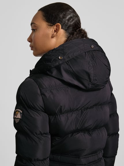 Frauenmodel trägt Steppmantel mit Pattentaschen von Superdry in Schwarz, Kapuze mit Kunstfell, Detailaufnahme Rückansicht.