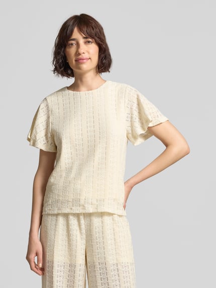 Frauenmodel trägt Kurzarmbluse mit Lochstickerei Modell 'CASSANDRA' von Vero Moda, Optik: Unifarben, Regular-Fit, Rundhals, Ärmelform: Kurzarm, Materialverarbeitung: Lochstickerei, helle Farbe, feine Textur, Ganzkörperansicht von vorne.