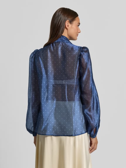 Frauenmodel trägt Schluppenbluse im semitransparenten Design von Rich & Royal, gepunkteter Stoff, blauer Ton, Ganzkörperansicht Rückansicht.