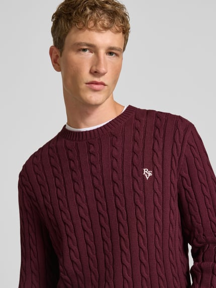 Männermodel trägt Slim Fit Strickpullover aus reiner Baumwolle mit Zopfmuster von REVIEW, weinrot, Label-Stitching, Nahaufnahme Oberkörper.