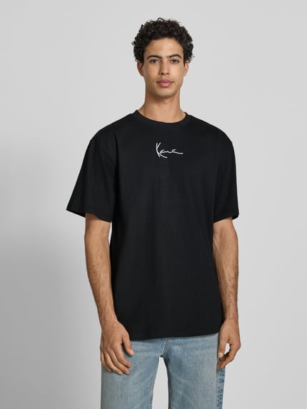 Männermodel trägt T-Shirt mit Label-Stitching und Rundhalsausschnitt von KARL KANI, Oversized, Reine Baumwolle, Rückenlänge 77 cm, Ganzkörperansicht von vorne.