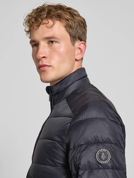 Männermodel trägt Regular Fit Jacke in Stepp-Optik Modell 'Kingsley' von JACK & JONES in Dunkelgrau, Nahaufnahme Oberkörper. Rückenlänge 72 cm, Schulterbreite 48 cm, Brustweite 51 cm, Ärmellänge 68 cm, Stehkragen, Reißverschluss, Eingrifftaschen.