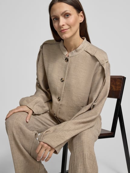 Frauenmodel trägt Jacke aus Viskose-Mix mit Stehkragen Modell 'RINA' von YAS, Relaxed-Fit, Knopfleiste, Eingrifftaschen, Nahaufnahme Oberkörper. Rückenlänge Größe 36: 54 cm, Schulterbreite: 48 cm, Brustweite: 57 cm, Ärmellänge: 61 cm, Stretch-Anteil, beige textured Oberfläche.