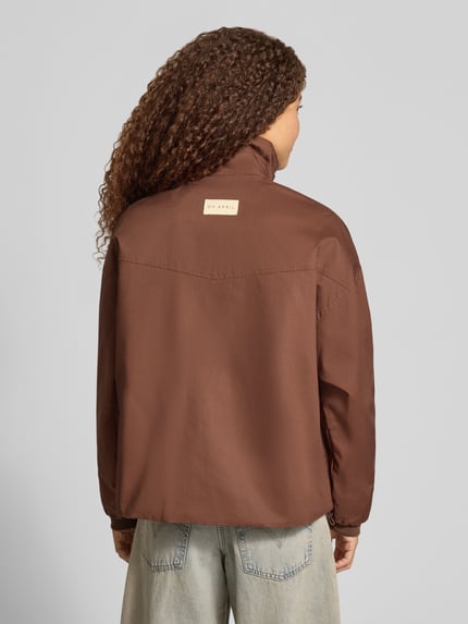 Frauenmodel trägt Wendejacke aus reiner Baumwolle Modell 'Amine' von OH APRIL in Braun, lockere Form, glatte Textur, Ganzkörperansicht Rückansicht. Rückenlänge 64 cm, Schulterbreite 44 cm, Brustweite 58 cm, Ärmellänge 54 cm, Stehkragen, Eingrifftaschen, gerippte Ärmelabschlüsse, beidseitig tragbar.