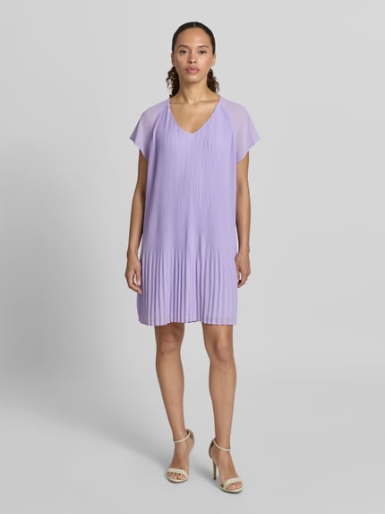 Frauenmodel trägt knielanges Cocktailkleid mit Plisseefalten Modell 'Inken' von GUIDO MARIA KRETSCHMER WOMAN in Flieder, Chiffon, Ganzkörperansicht von vorne.