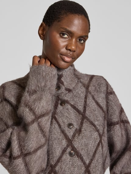 Frauenmodel trägt Strickjacke aus Alpaka mit Zierknöpfen Modell 'Dargyle' von OPUS in brauner Gitterkaro-Strickoptik, Nahaufnahme Oberkörper.