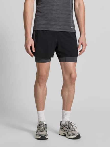 Männermodel trägt Regular Fit Shorts mit integrierten Tights Modell 'Road' von ASICS TIGER in Schwarz mit elastischem Bund, Ganzkörperansicht von vorne.