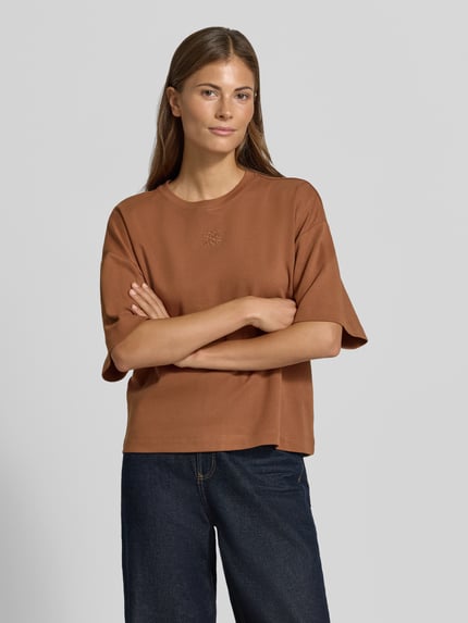 Frauenmodel trägt Oversized T-Shirt aus reiner Baumwolle von s.Oliver RED LABEL in Braun, kombiniert mit dunkler Jeans, Ganzkörperansicht von vorne.