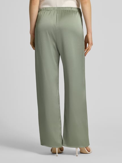 Frauenmodel trägt Wide Fit Hose aus Satin von Calvin Klein Womanswear in einfarbigem Hellgrün, elastischer Bund, Ganzkörperansicht Rückansicht.