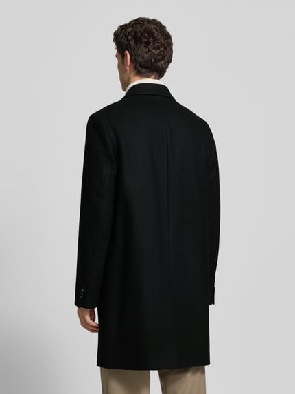 Männermodel trägt Wollmantel mit Label-Schriftzug Modell 'Malte2641' von HUGO, regular fit, look: effen, lange mouw, reverskraag, eenrijige knoopsluiting, loopsplit, steekzakken, geknoopte mouwboord, longline lengte, labelopschrift applicatie, ganzkörperansicht rückansicht.