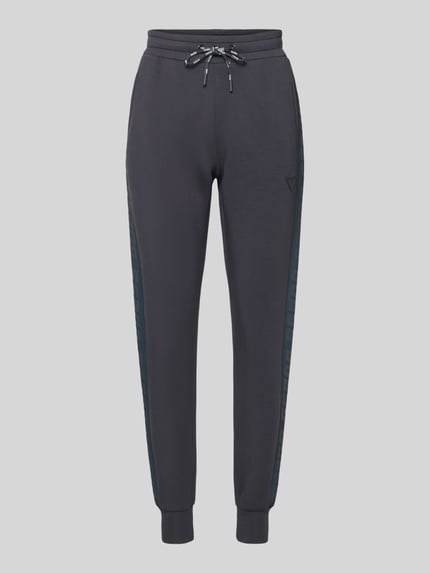 Produktfoto, dunkelgraue Sweatpants mit elastischem Bund Modell 'ALLIE' von Guess, lockerer Schnitt, seitliche Zierstreifen, Viskose-Mix mit Stretch-Anteil, sichtbarer Tunnelzug und französische Eingrifftaschen, sportliche Textur.
