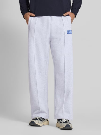 Mężczyzna nosi spodnie dresowe Sweatpants mit elastischem Bund und Label-Print von Carhartt Work In Progress, bawełna, model 'Pond Corps', krój wide leg, elastyczny pas, szwy pionowe, nadruk z logo, długość wewnętrzna nogawki w rozmiarze M: 72 cm, Ganzkörperansicht von vorne.