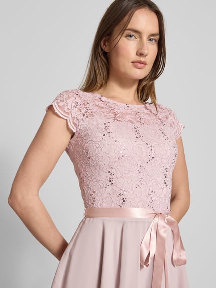 Vrouwenmodel draagt Cocktailjurk met kanten details en strikceintuur van SWING, lichtroze, A-lijn, mix van materialen, pailletten, detailopname bovenlichaam.