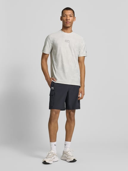 Männermodel trägt T-Shirt mit Rundhalsausschnitt und Label-Detail von EA7 Emporio Armani, Material-Mix mit Stretch-Anteil, Regular-Fit, dezente Farben, glatte Textur, Rückenlänge bei Größe M 69 cm, Ganzkörperansicht von vorne.